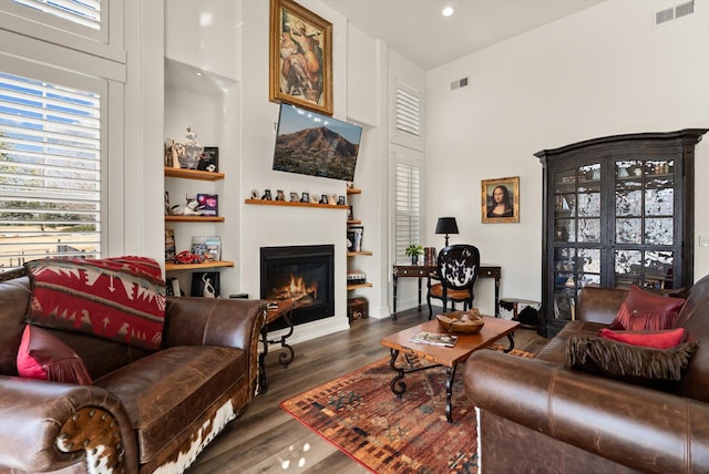 living room with a healthy amount of sunlight, visible vents, wood finished floors, and a glass covered fireplace