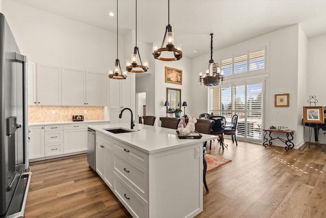 kitchen with appliances with stainless steel finishes, a sink, light wood finished floors, and a high ceiling