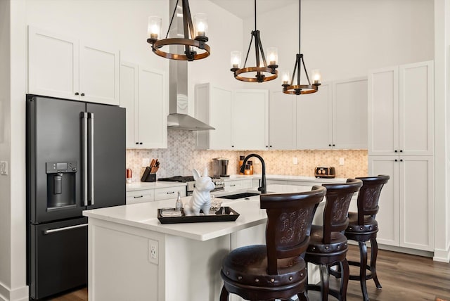 kitchen with light countertops, backsplash, a sink, high end black refrigerator, and wall chimney exhaust hood