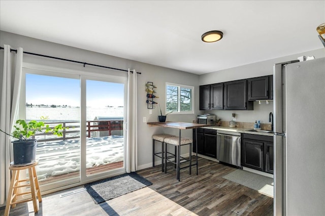 kitchen featuring dark wood finished floors, dark cabinets, stainless steel appliances, light countertops, and a sink