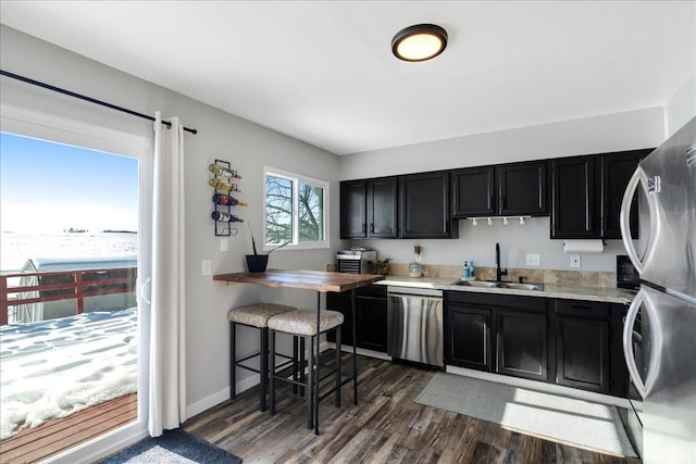 kitchen with dark cabinets, dark wood-style flooring, stainless steel appliances, light countertops, and a sink