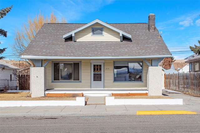 bungalow-style house with covered porch, roof with shingles, a chimney, and fence