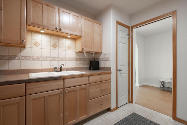 kitchen featuring light brown cabinets, a sink, baseboards, light floors, and tasteful backsplash