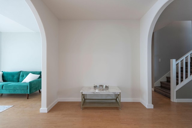 interior space featuring light wood finished floors, stairway, baseboards, and arched walkways