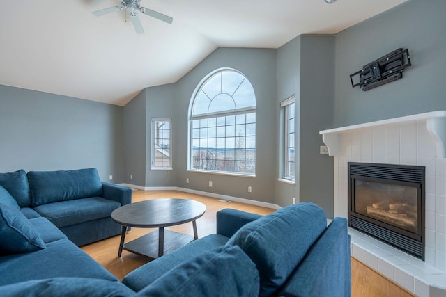 living room with lofted ceiling, wood finished floors, visible vents, baseboards, and a tiled fireplace