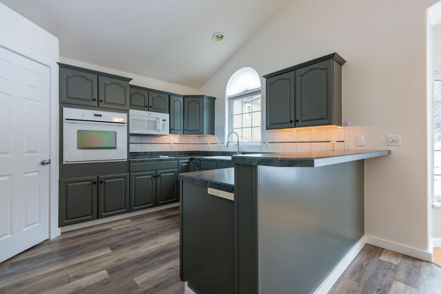 kitchen featuring white appliances, dark countertops, a peninsula, vaulted ceiling, and backsplash