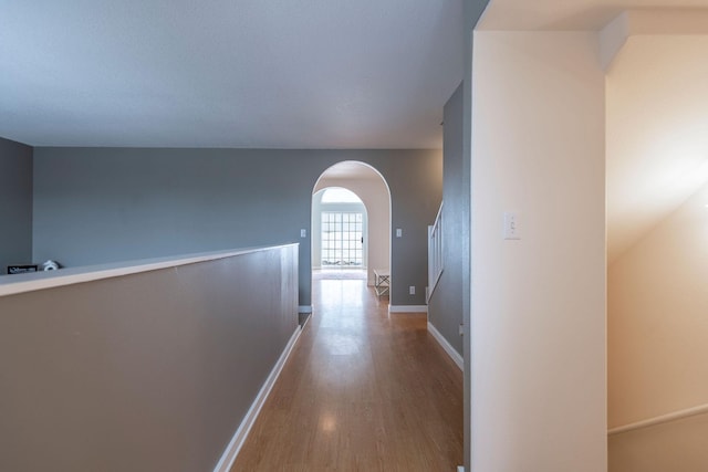 corridor with baseboards, arched walkways, and wood finished floors