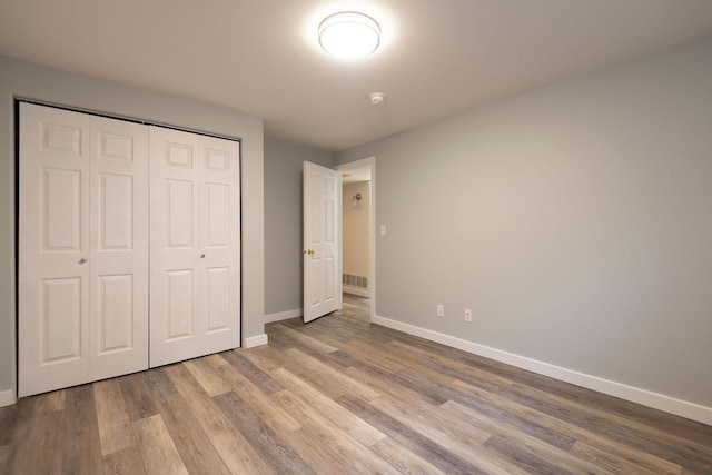 unfurnished bedroom featuring a closet, wood finished floors, visible vents, and baseboards