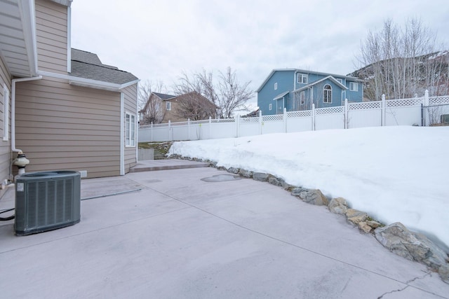 snow covered patio featuring central AC and a fenced backyard