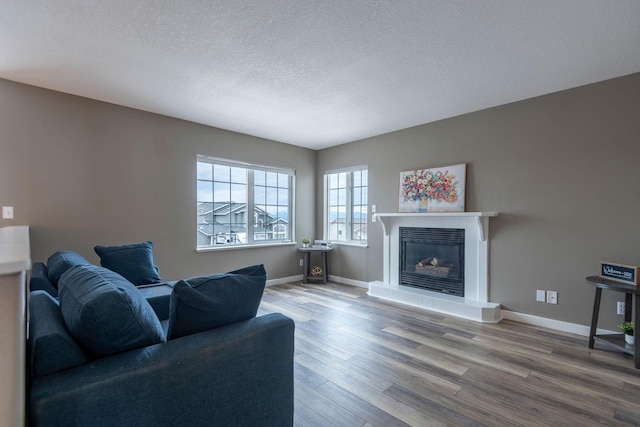 living area featuring a tile fireplace, a textured ceiling, baseboards, and wood finished floors