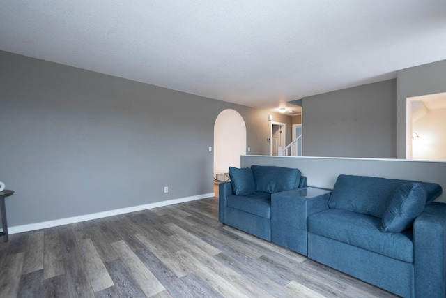 living room with arched walkways, baseboards, and wood finished floors