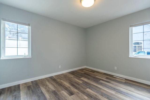 spare room with visible vents, baseboards, dark wood-type flooring, and a wealth of natural light