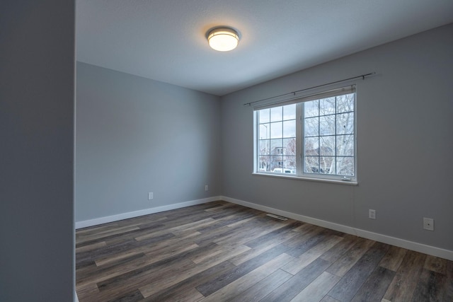 spare room featuring dark wood-style floors, visible vents, and baseboards