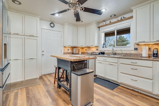 kitchen with a sink, backsplash, light wood finished floors, and wood counters