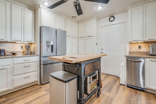 kitchen with light wood finished floors, tasteful backsplash, appliances with stainless steel finishes, white cabinets, and a ceiling fan