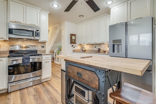 kitchen with tasteful backsplash, appliances with stainless steel finishes, light wood-style flooring, and butcher block counters