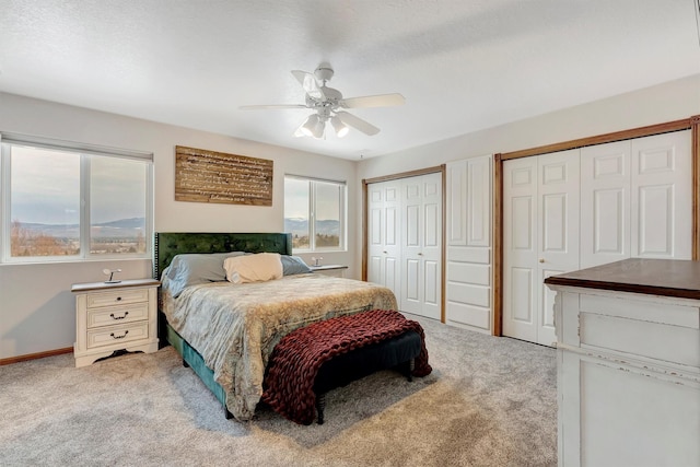 bedroom featuring light carpet, baseboards, a ceiling fan, and multiple closets