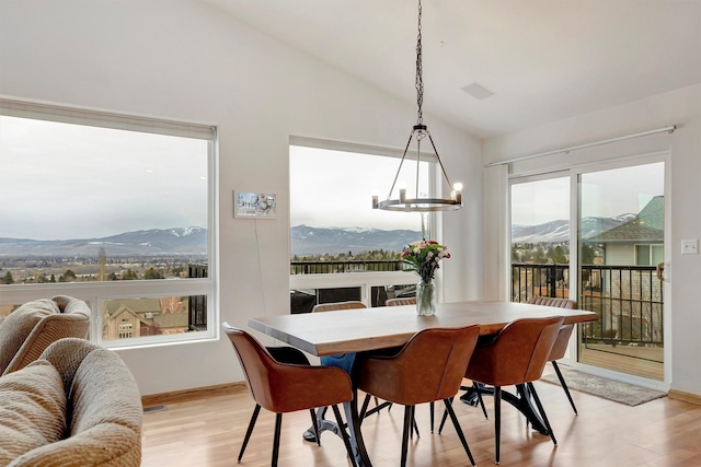 dining room featuring light wood finished floors, baseboards, a chandelier, lofted ceiling, and a mountain view