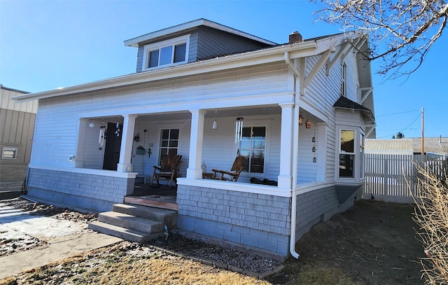 view of front of home with covered porch, a chimney, and fence