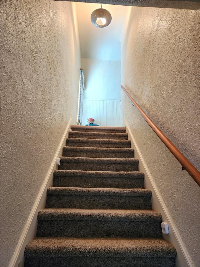 stairway with wainscoting and a textured wall