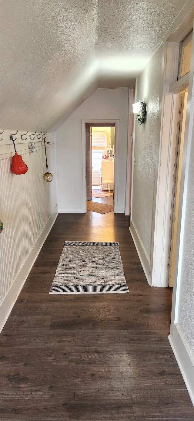 hallway with vaulted ceiling, a textured ceiling, and wood finished floors