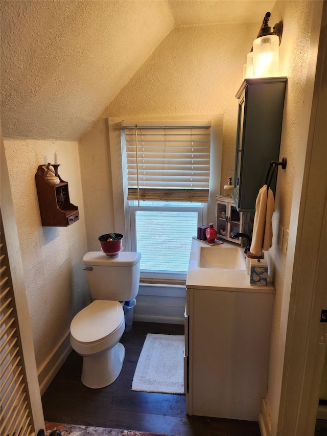 half bathroom with lofted ceiling, toilet, wood finished floors, and a textured wall