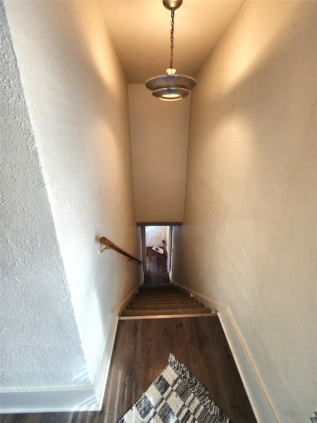 stairway with a textured wall, baseboards, and wood finished floors