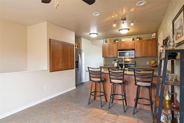 kitchen with brown cabinetry, appliances with stainless steel finishes, a breakfast bar, a peninsula, and tile patterned flooring