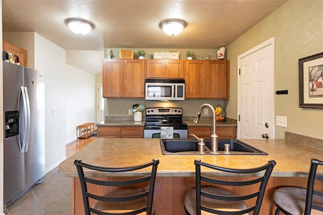 kitchen with stainless steel appliances, brown cabinetry, a sink, and a kitchen bar