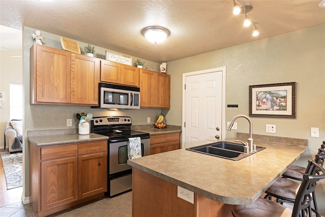 kitchen featuring a breakfast bar area, appliances with stainless steel finishes, a sink, a textured ceiling, and a peninsula