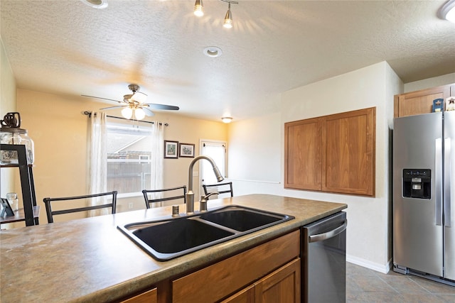 kitchen featuring stainless steel appliances, brown cabinets, a sink, and a ceiling fan