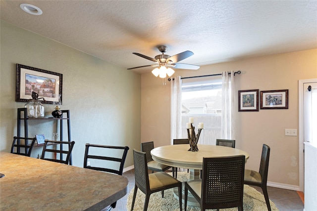 tiled dining area featuring a ceiling fan, a textured ceiling, and baseboards