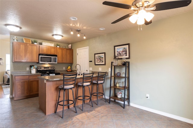 kitchen featuring a peninsula, a kitchen bar, appliances with stainless steel finishes, and brown cabinetry