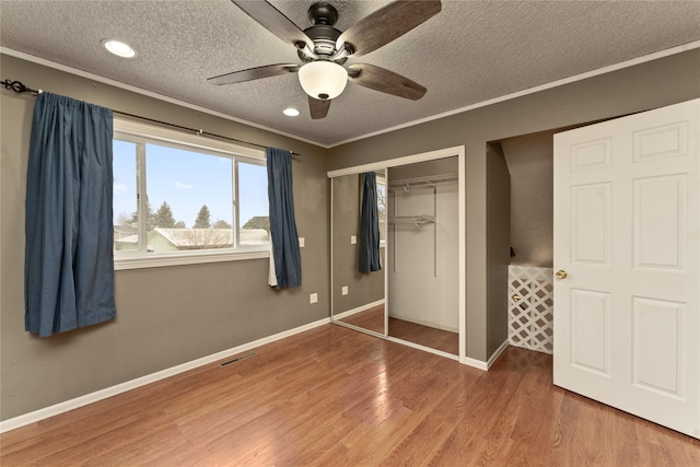 unfurnished bedroom with crown molding, a closet, a textured ceiling, wood finished floors, and baseboards