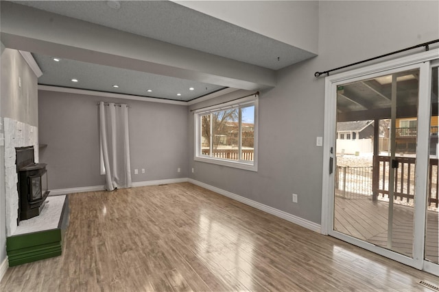 unfurnished living room featuring recessed lighting, wood finished floors, a wood stove, and baseboards