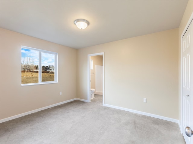 unfurnished bedroom featuring ensuite bathroom, a closet, and baseboards