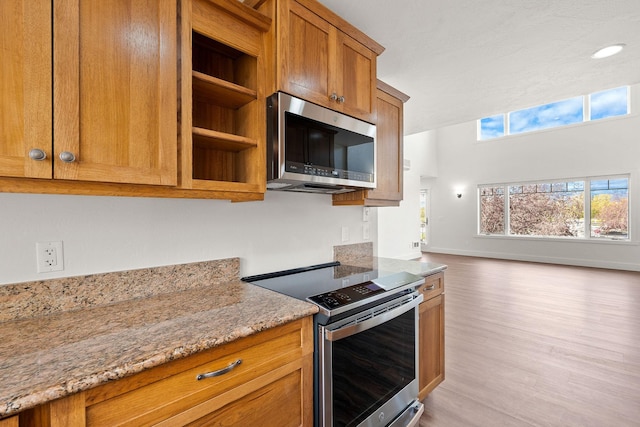 kitchen featuring stainless steel appliances, light wood-type flooring, brown cabinets, and light stone countertops