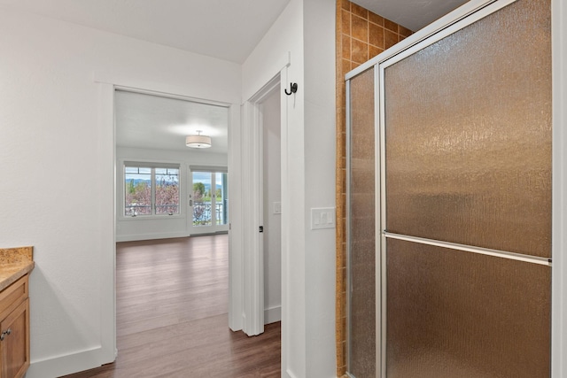 bathroom with a stall shower, wood finished floors, vanity, and baseboards