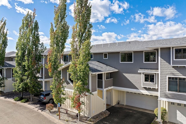 view of property featuring a garage, a shingled roof, a residential view, and aphalt driveway