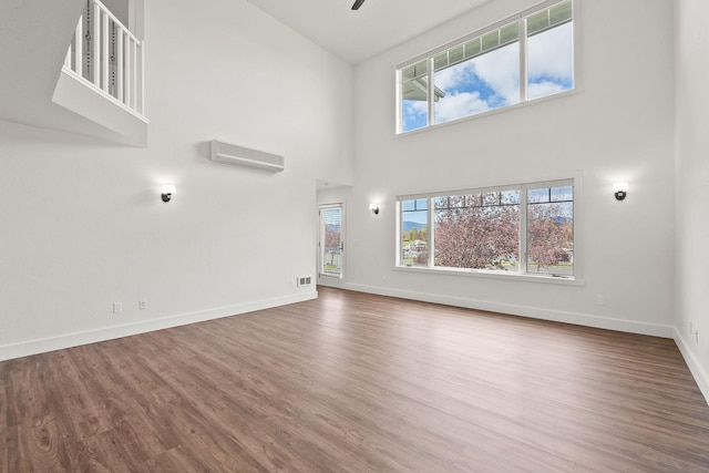 unfurnished living room featuring a wealth of natural light, an AC wall unit, and wood finished floors