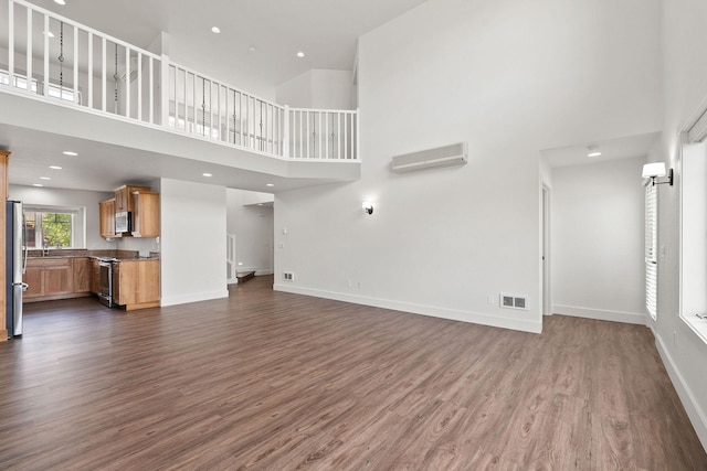 unfurnished living room featuring dark wood finished floors, visible vents, a towering ceiling, a wall mounted AC, and baseboards