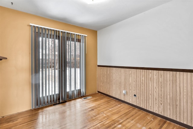 empty room with wood walls, visible vents, wood finished floors, and wainscoting