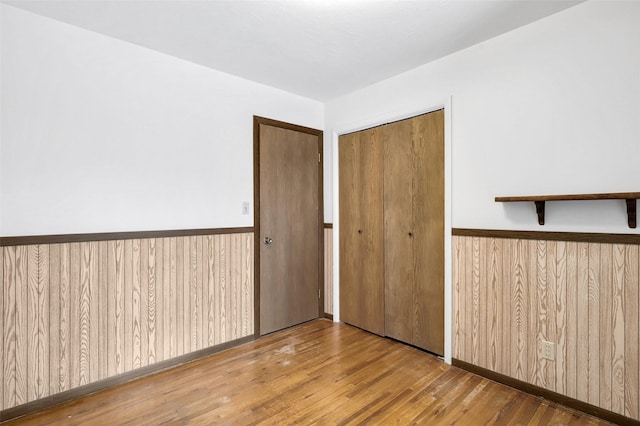 unfurnished bedroom featuring a closet, wood-type flooring, a wainscoted wall, and wooden walls