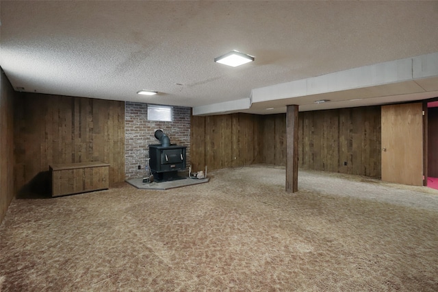 finished below grade area featuring a textured ceiling, wood walls, carpet, and a wood stove