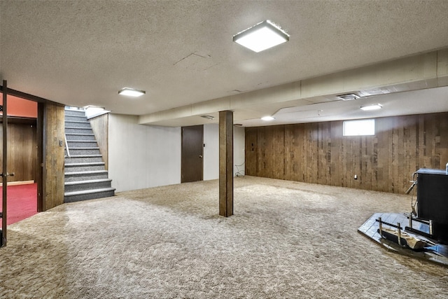 basement featuring wood walls, stairs, carpet flooring, and a textured ceiling