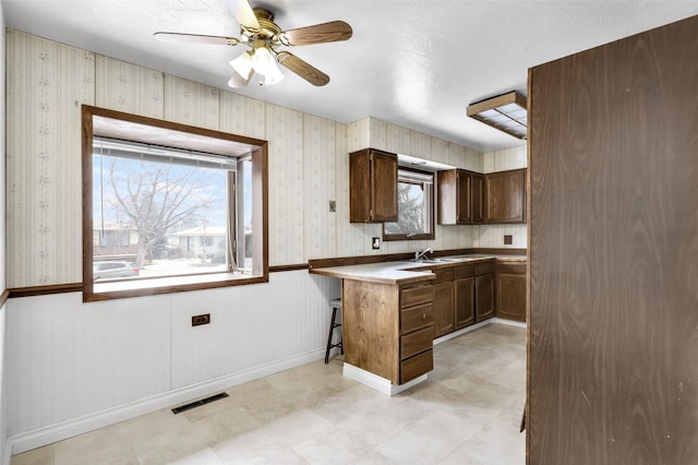 kitchen with ceiling fan, a breakfast bar area, a peninsula, visible vents, and wallpapered walls