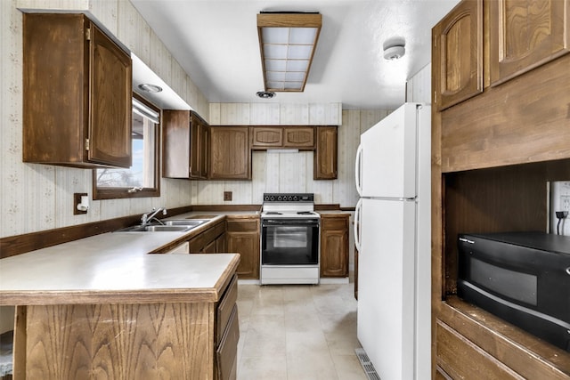 kitchen featuring wallpapered walls, freestanding refrigerator, a peninsula, a sink, and range with electric stovetop