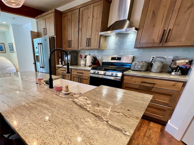 kitchen with light stone counters, stainless steel appliances, wood finished floors, decorative backsplash, and wall chimney exhaust hood