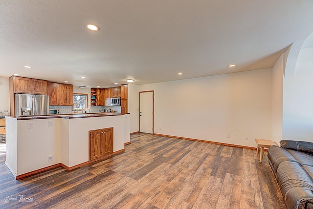 kitchen featuring open floor plan, stainless steel appliances, dark wood-type flooring, and brown cabinets