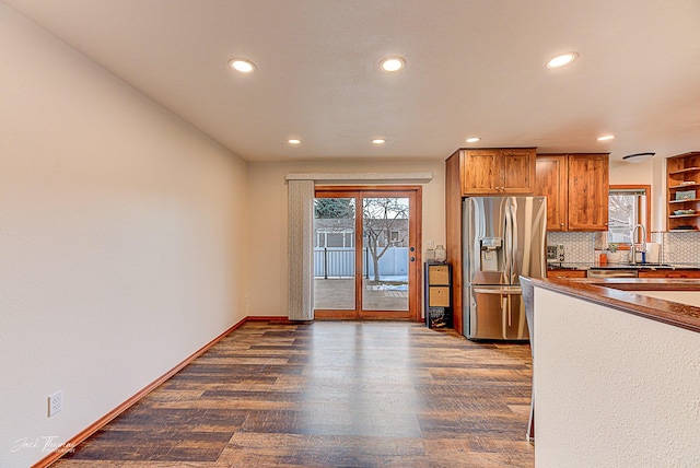 kitchen with dark wood-style flooring, baseboards, backsplash, brown cabinetry, and stainless steel fridge